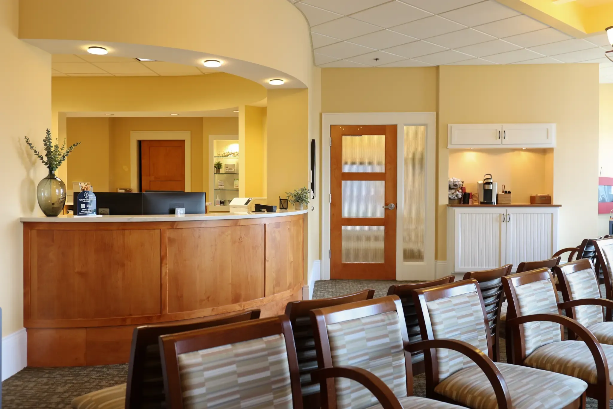 The Grandville Dental reception desk and waiting area, with warm yellow walls and upholstered seating